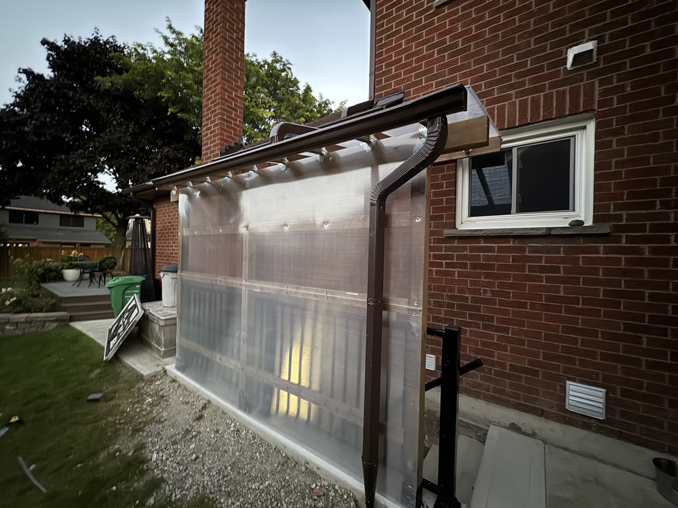 Polycarbonate basement canopy for snow protection against a brick house at dusk