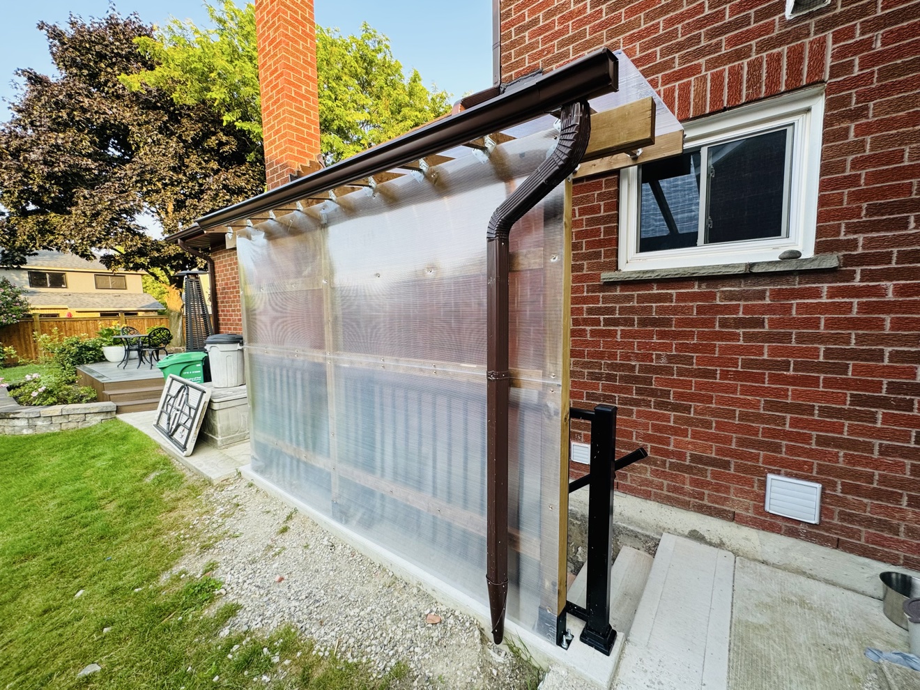 Polycarbonate basement canopy for snow protection against a brick house in daylight